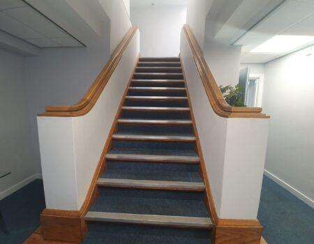 Carpeted staircase fitting with white decor and wooden trim installed in an apartment hallway lobby by Top Drawer Construction Woking Surrey